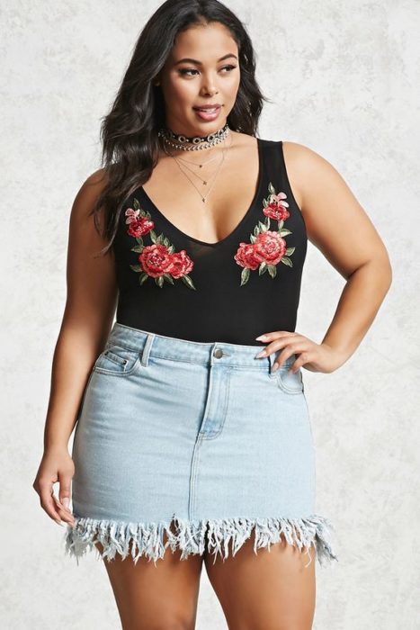 Chica curvy usando mini falda denim, con blusa sin mangas con estampado de flores en escote U