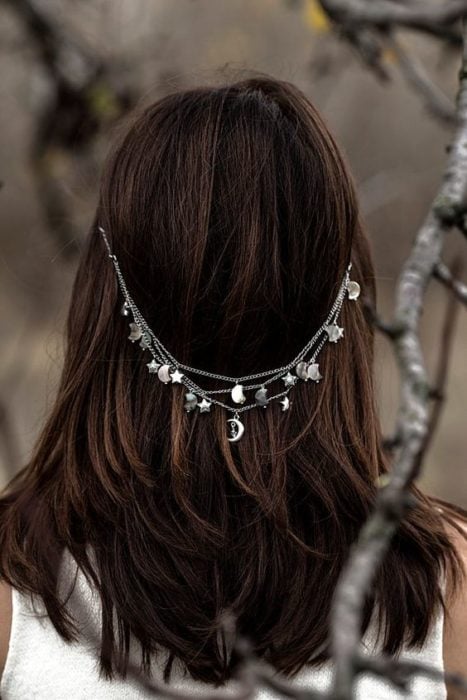 Mujer de espaldas con cabello suelta usando una cadena plateada con detalles de luna y estrellas