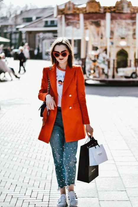 Chica usando blazer de color ladrillo, con blusa blanca y jeans denim con perlitas y tenis