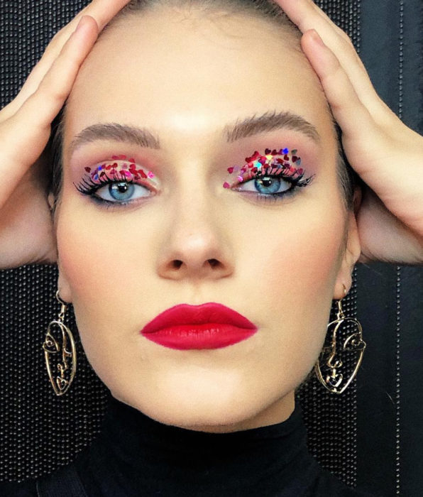 Mujer de ojos azules con maquillaje femenino natural, sombra glitter brillos, labial rojo duerte