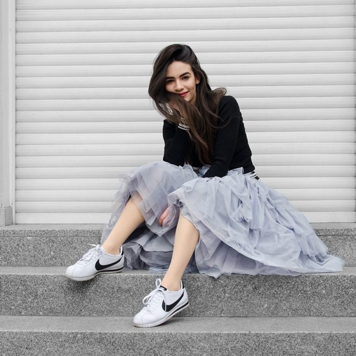 Chica usando falda de tul color gris y suéter negro y tenis blancos