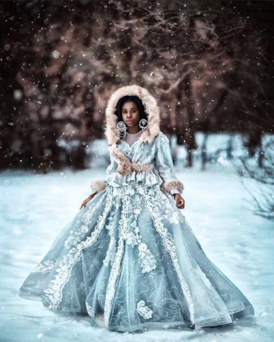 Chica negra en la nieve con vestido azul claro con capucha