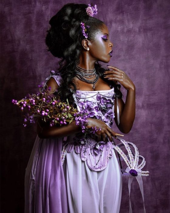 Mujer negra con vestido lila y detalles morados sosteniendo un remos de flores moradas