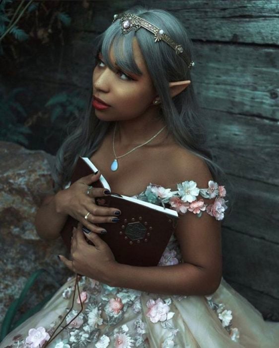 Mujer negra con cabello gris y orejas de elfo con vestido floreado sosteniendo un libro