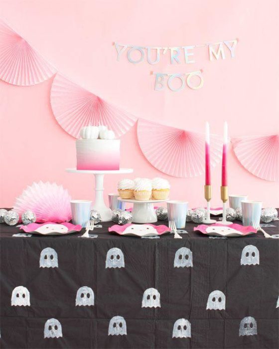 Mesa de dulces para Halloween con mantel negro con fantasmitas y pared rosa pastel