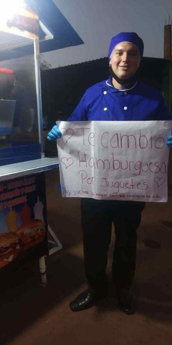 Chico con filipina azul sosteniendo un letrero intercambiando hamburguesas por juguetes para niño indígenas