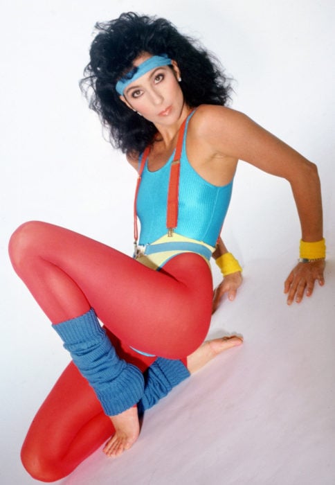 Looks icónicos de Cher; atuendo retro para hacer ejercicio, leggin rojo, calentadores azules, cabello negro, esponjado y chino
