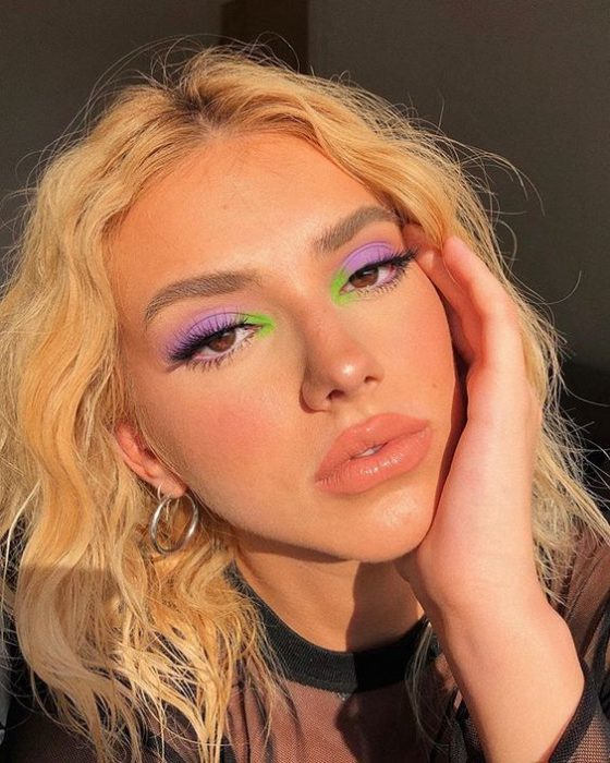 Chica rubia de cabello rizado con maquuillaje de ojos morado con toque de color verde y labios nude