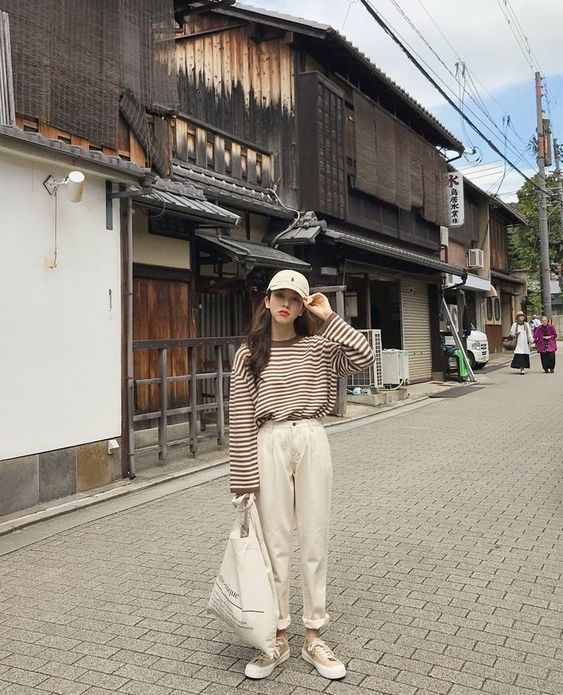 Chica asiática con cabello largo con gorra beige, blusa de manga larga beige con rayas cafés y pantalón beige oversized