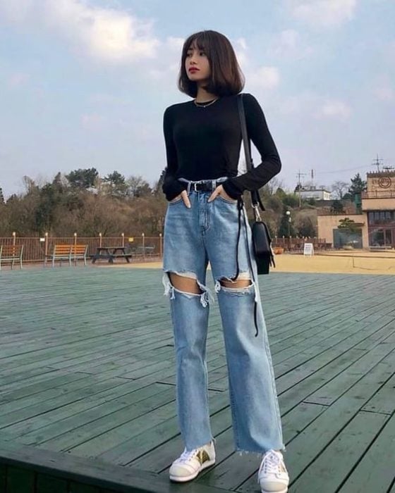 Chica asiática con melena corta con blusa negra de manga larga y pantalón de mezclilla roto