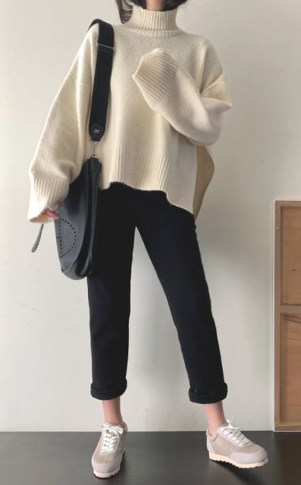 Chica asiática con suéter largo beige y pantalón negro con bolsa negra grande