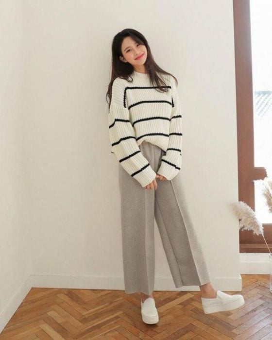 Chica asiática con sueter grande blanco con rayas negras y pantalón gris amplio 