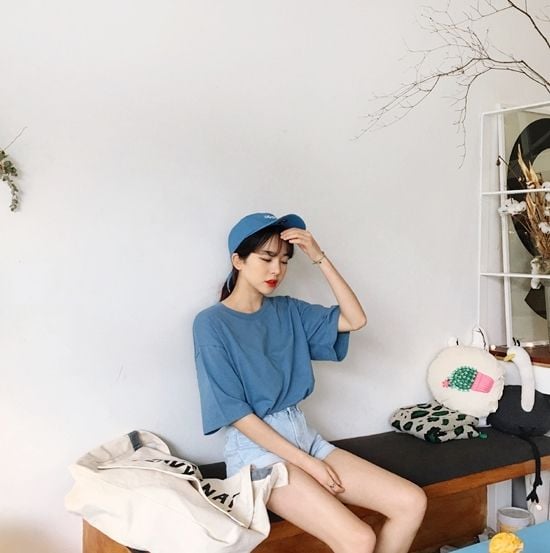 Chica asiática sentada con gorra y blusa color azul y shorts claro de mezclilla