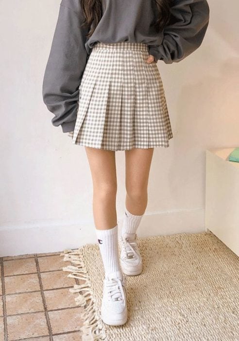 Chica asiática con falda de tablas color beige con cuadros con calcetas y tenia blancos