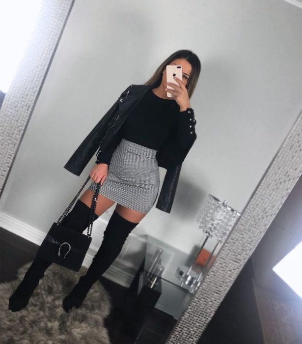 Chica usando chaqueta de cuero negra con botas altas, falda gris y blusa negra