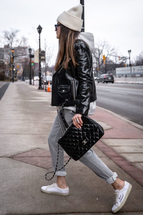 Chica usando chaqueta de cuero negra con pantal+ón gris, tenis blancos, y gorro blanco