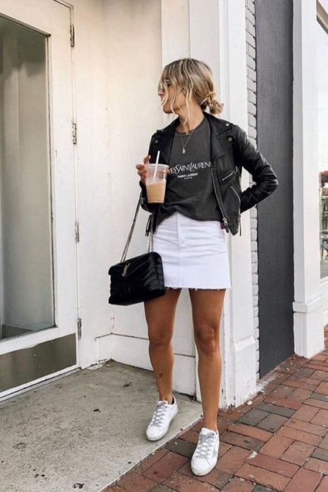 Chica usando chaqueta de cuero negra con falda y tenis blancos y playera holgada gris