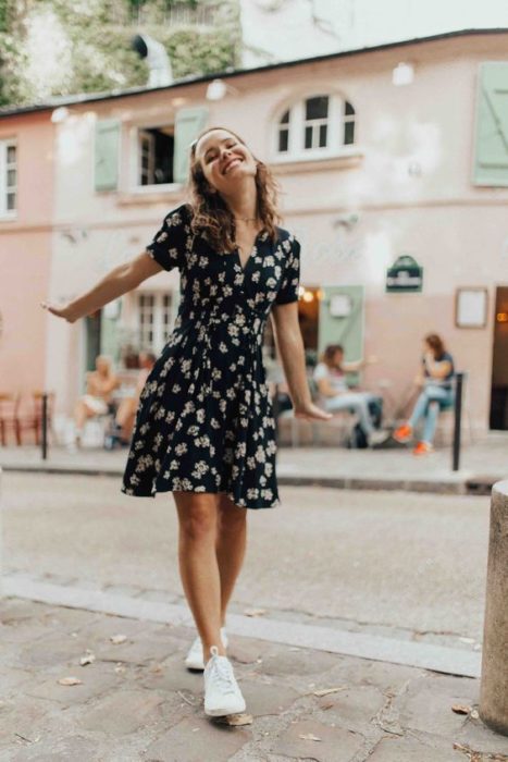 Chica usando outfit veraniego de vestido azul marino con estampado y arriba de la rodilla, usando tenis blancos