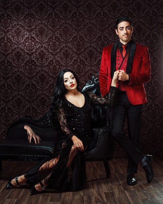 Pareja recreando escena de la película Los locos Addams, sostenidos de las manos y llevando ropa oscura