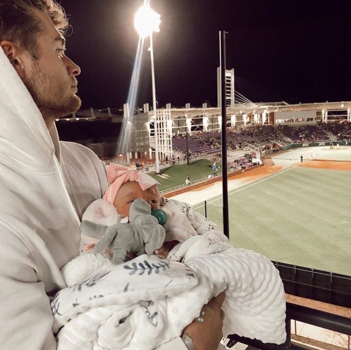 Padre sosteniendo en brazos a bebé en un estadio de futbol