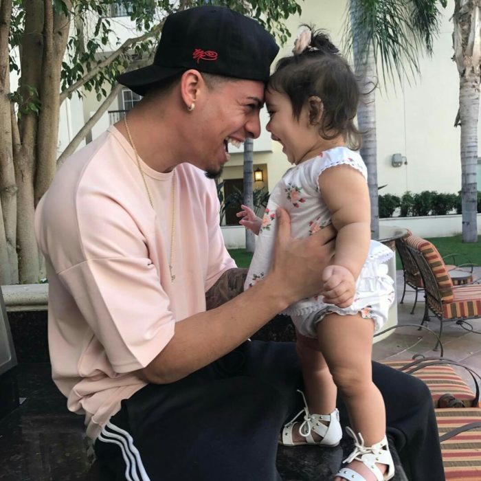 Padre con gorra negra y playera rosa sosteniendo a su bebé en brazos