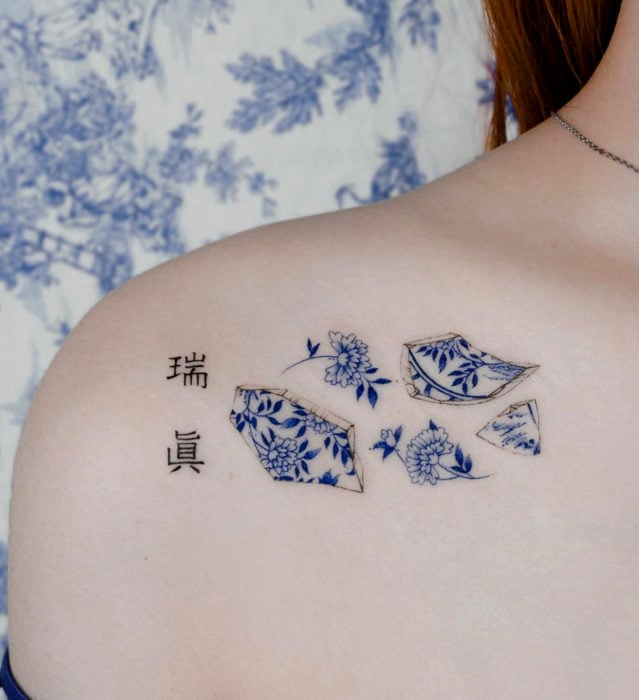Tatuaje pequeño estilo japonés de tinta azul de plato de cerámica porcelana roto kanjis en el hombro