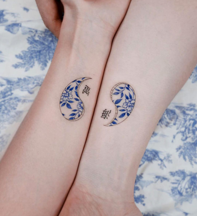 Tatuaje pequeño estilo japonés de tinta azul de yin yang con flores en las muñecas