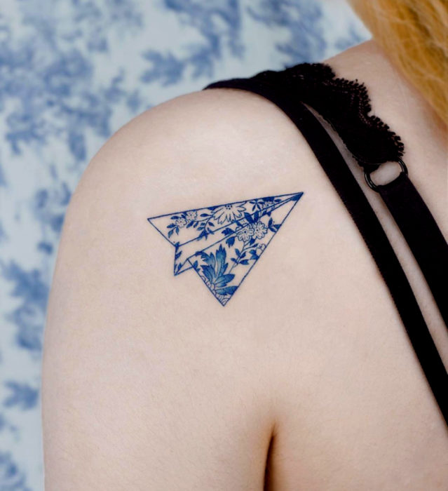 Tatuaje pequeño estilo japonés de tinta azul de avión de papel con flores en el hombro