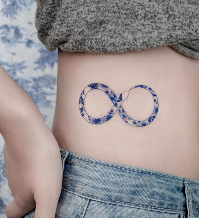 Tatuaje pequeño estilo japonés de tinta azul de serpiente comiendo su cola con flores en la cintura
