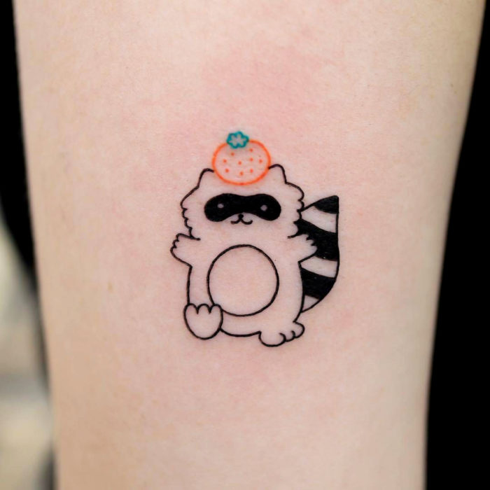 Tatuaje tierno kawaii en el brazo, mapache con naranja