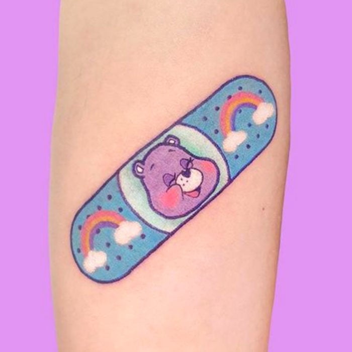 Tatuaje tierno kawaii en el brazo, curita de Los ositos cariñositos, oso morado con arcoíris