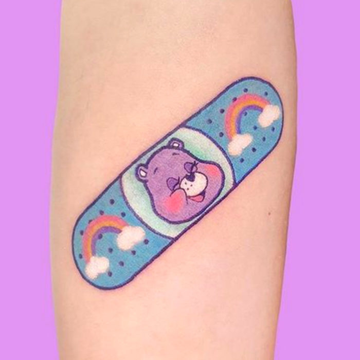 Tatuaje tierno kawaii en el brazo, curita de Los ositos cariñositos, oso morado con arcoíris