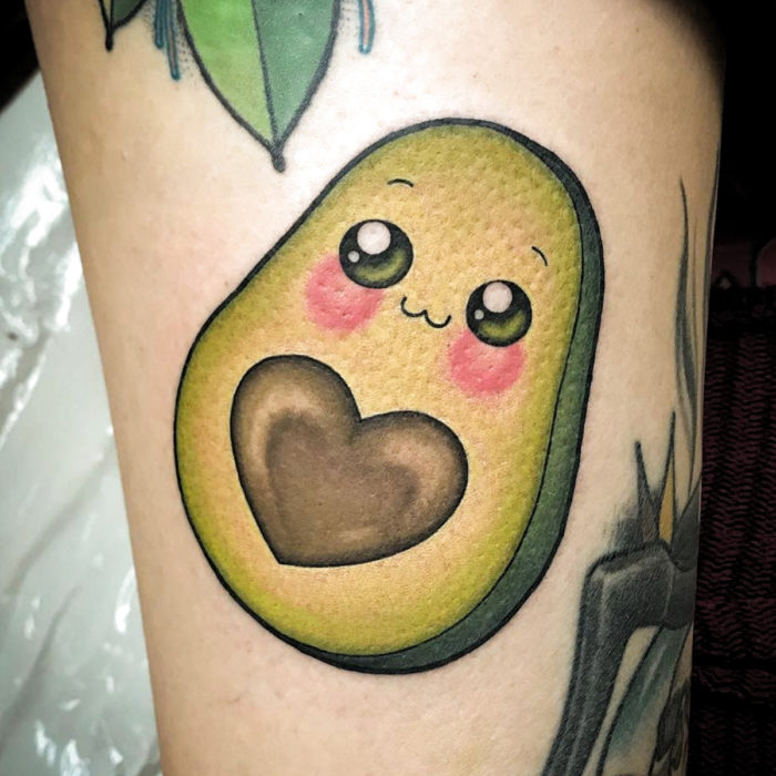 Tatuaje tierno kawaii en el brazo de aguacate lindo con cara feliz y semilla en forma de corazón