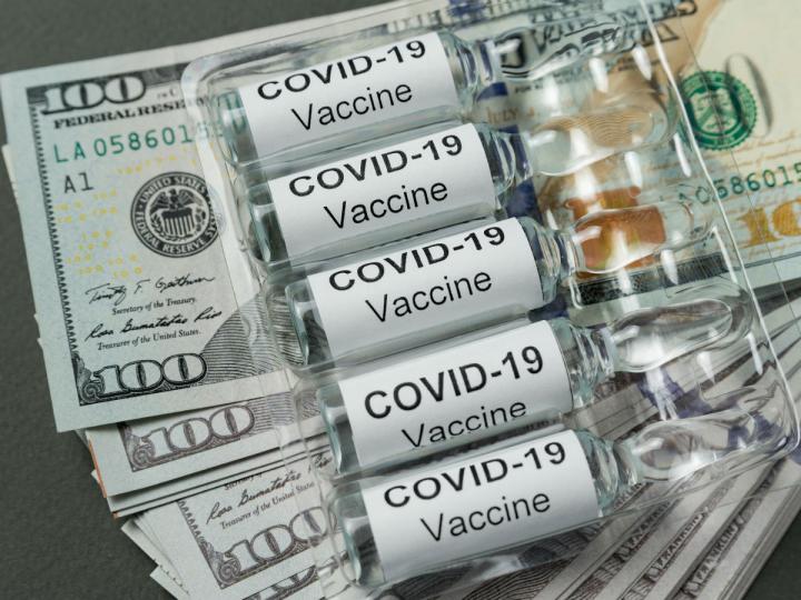 Ampolletas de vacunas contra Covid-19 y dólares debajo de ellas