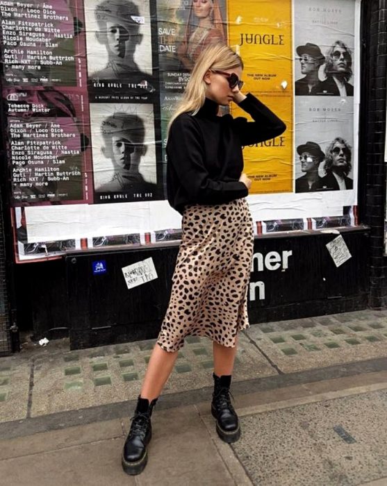 chica rubia usando lentes de sol, suéter negro de cuello alto, vestido de satén slip dress de animal print y botas de cuero negras