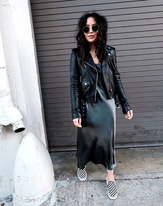 chica de cabello castaño largo con lentes de sol, chamarra de cuero, vestido de satén azul marino con tenis vans blanco y negro