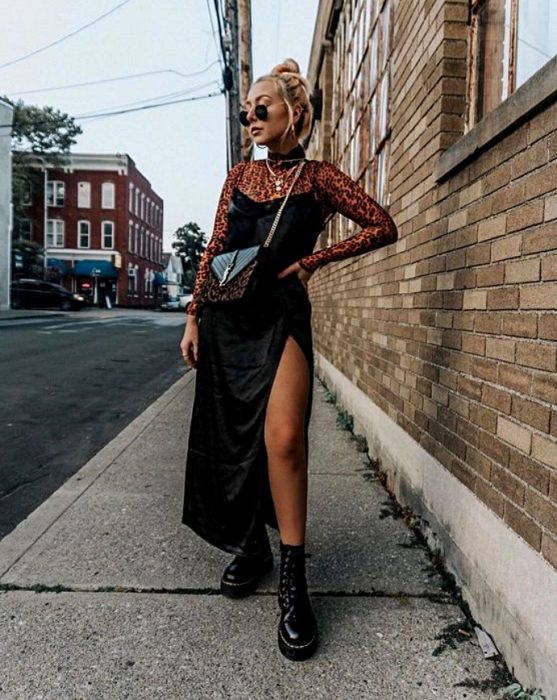 chica rubia usando un vestido negro de satén slip dress negro con blusa de mesh de manga larga, bolso pequeño y botas negras de cuero militares