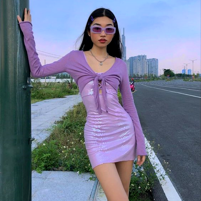 chica de cabello oscuro largo usando un cárdigan morado, un vestido lila y lentes de sol lilas
