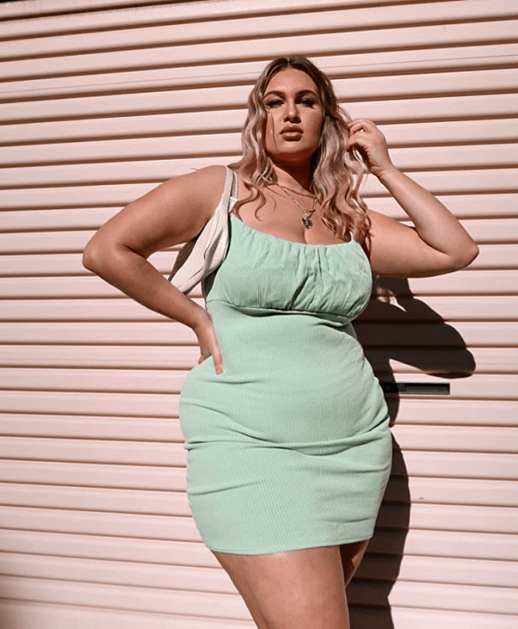 chica rubia curvy usando un vestido verde pistache ceñido con bolso de mano blanco