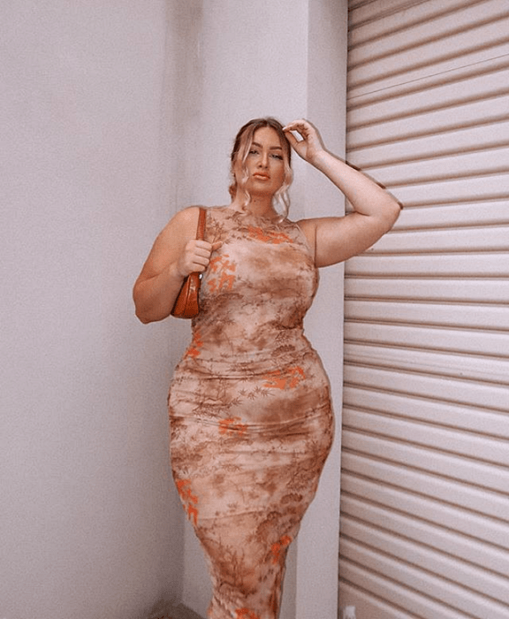 chica rubia curvy usando un vestido ceñido color nude con estampado de rosas y flores, usando bolso de mano color naranja