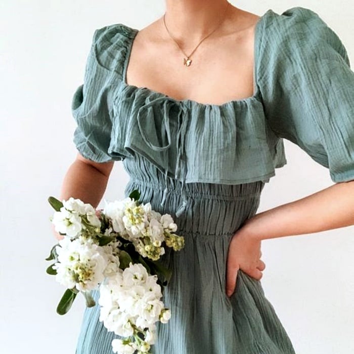 chica usando un vestido verde opaco gris con escote cuadrado y mangas de 3/4 sosteniendo unas flores blancas