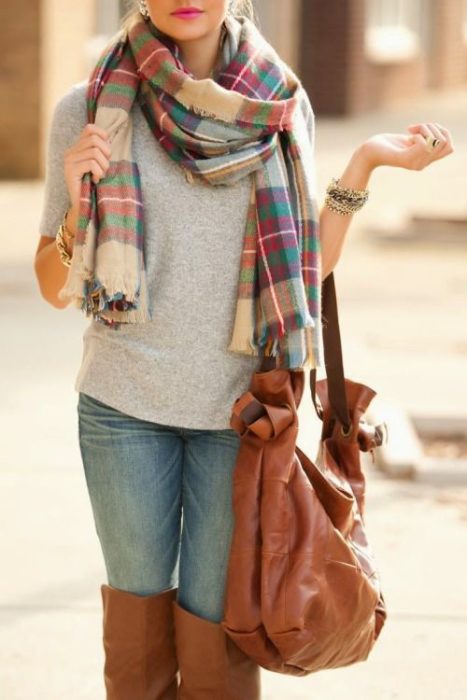 Chica usando jeans, suéter gris y bufanda de cuadros, junto con una bolsa de mano color camel