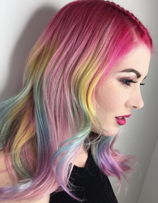 Mujer con maquillaje sencillo, cabello a los hombros, ondulado y teñido de colores arcoíris pastel, azul, verde, amarillo, rosa y morado, peinado con una trenza delgada