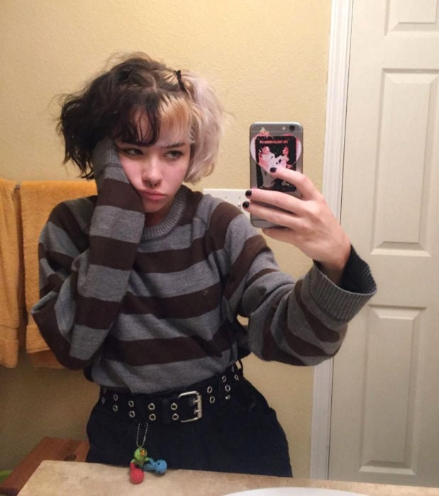 Looks aesthetic con cabello corto pintado mitad negro y blanco, con fleco; chica tomándose una selfie frente al espejo, con suéter rayado y estilo grunge