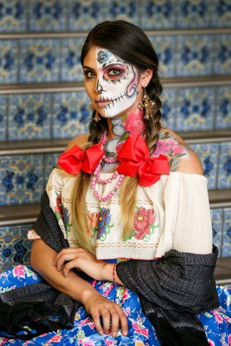 Maquillaje de catrina en la mitad del rostro, con peinado de dos trenzas a los lados