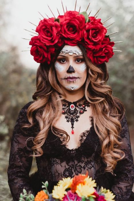 Maquillaje de catrina en rostro completo, con detalles en blanco y negro y tocado de rosas rojas sobre el cabello y este suelto