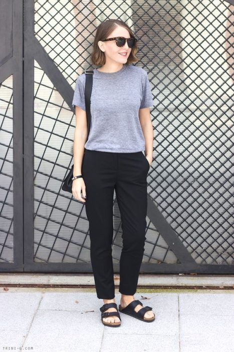 Chica con cabello corto castaño, pantalón negro, blusa gris y sandalias negras