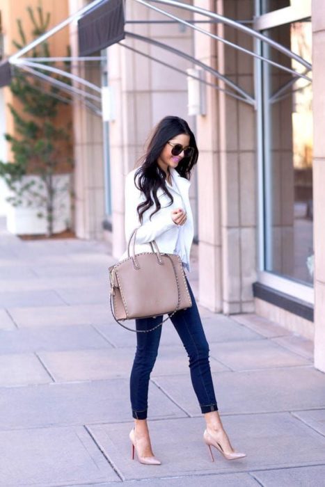 Mujer con saco blanco, bolsa beige, jeans oscuros y stilettos beige