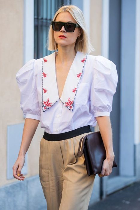 Chica rubia caminando en la calle con pantalón beige y blusa azul claro con cuello bobo