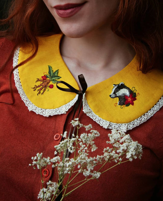 Little pin studio crea bonitos cuellos bordados de Halloween para vestidos y blusas; diseño de Hufflepuff, mandrágora, tejón sobre rela amarilla; mujer pelirroja con blusa anaranjada sonriendo